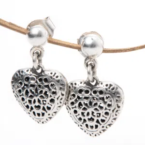Handcrafted silver filigree heart earrings hang from a fabric rope.