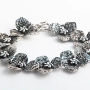 Handcrafted silver bracelet that is foamed with multiple orchid bloom flowers. Each flower has 3 petals formed with are raised circles and the centers a detailed mini flower with 5 petals.