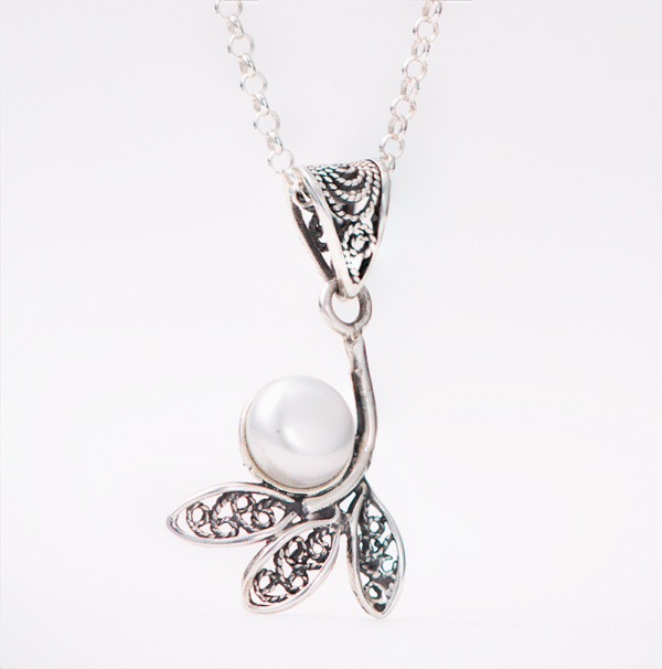 A handcrafted silver necklace with a pearl centerpiece hanging from a filigree style hook.