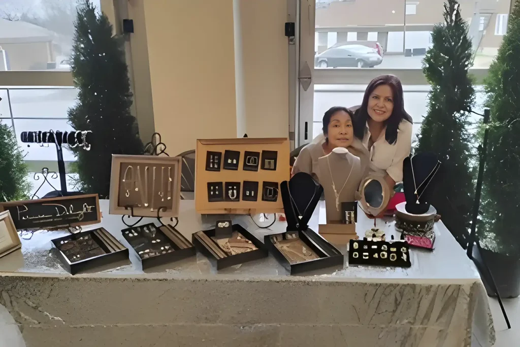 Two women stand behind a table that showcases tens of pieces of various jewelry at an event.