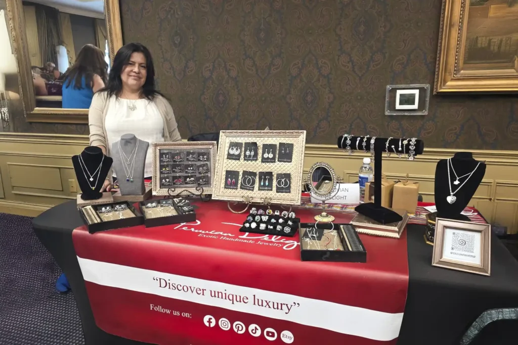 A woman stands behind a table that showcases tens of pieces of various jewelry at an event.